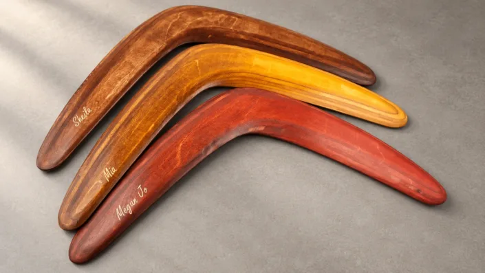 Personalized boomerangs in three colours — illustration Illustration of three wooden boomerangs in brown, amber and red with individual engraved names.