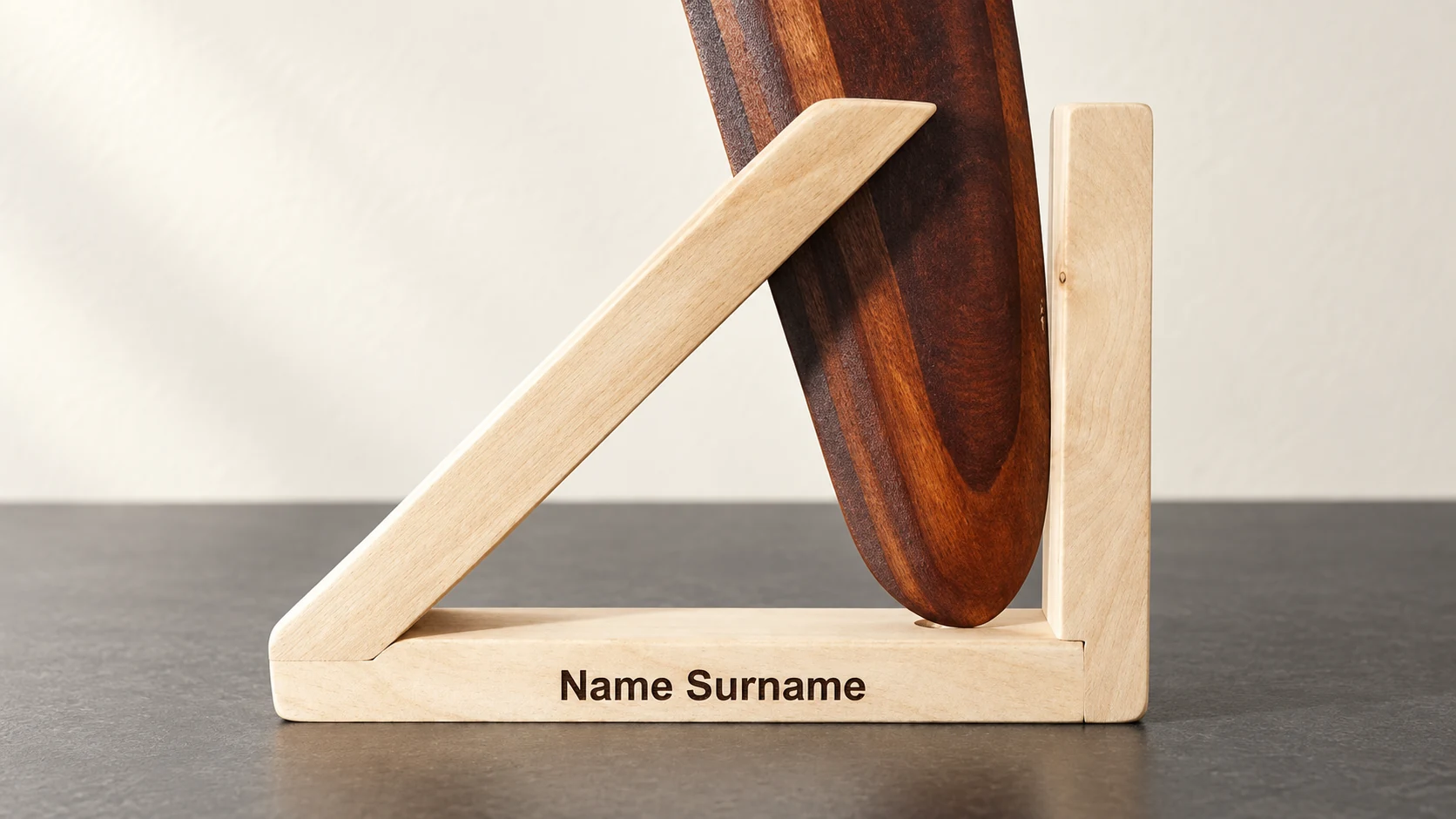 Name engraving on a wooden stand — illustration Illustration of a pale wooden boomerang stand engraved with the example text Name Surname.