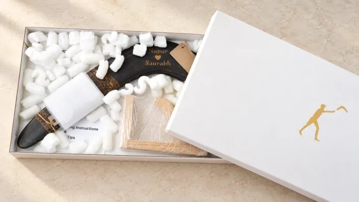 Boomerang and stand packed in a white gift box — illustration Illustration of an engraved boomerang and wrapped wooden stand in a white gift box with protective cushioning.