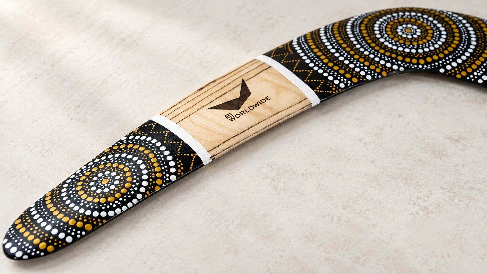 03-silver-sun-corporate-logo Illustration of a Silver Sun boomerang with an engraved BI WORLDWIDE logo and white and gold dotted decoration.