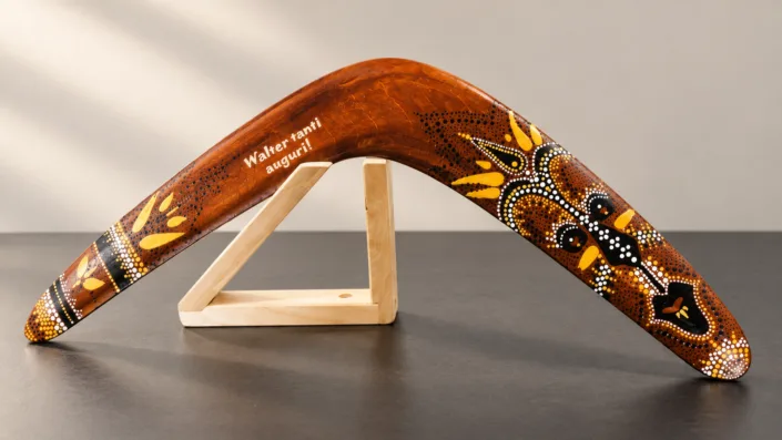 05-personalized-boomerang-on-stand Illustration of a personalized decorated wooden boomerang on a pale triangular wooden stand.