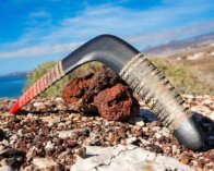 Authentic Baltic Birch - Built for Outdoors Tribal Ember wooden boomerang resting on rough volcanic rocks, showing the durable finish and wood grain.