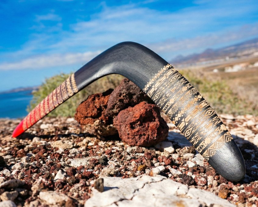 Authentic Baltic Birch - Built for Outdoors Tribal Ember wooden boomerang resting on rough volcanic rocks, showing the durable finish and wood grain.
