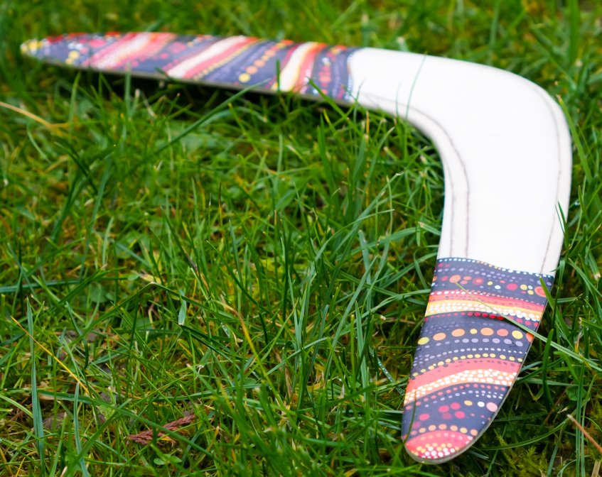 Golden Swallow returning boomerang lying flat on green grass displaying detailed aboriginal-style dot painting.