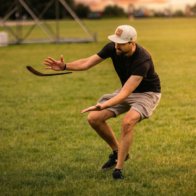 Man successfully catching a returning wooden boomerang in a grassy field.