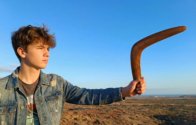 Teenager holding the Dark Brown Cedar boomerang against a blue sky looking at the horizon.