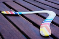 Handcrafted Skybreaker Wooden Boomarang The beautifully painted Skybreaker handcrafted wooden boomarang resting flat on a dark slatted table.