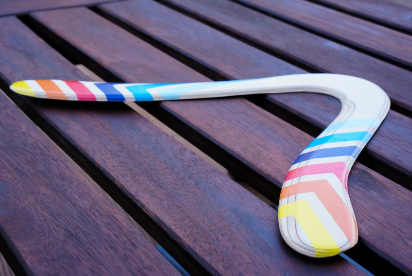 Handcrafted Skybreaker Wooden Boomarang The beautifully painted Skybreaker handcrafted wooden boomarang resting flat on a dark slatted table.