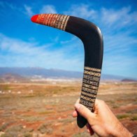 Unique Gift for Men - Handcrafted Detail Close-up of a man's hand holding the Tribal Ember boomerang, highlighting the red painted tip and engraved tribal design.