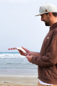 Profile view of a man inspecting the edge and finish of the Golden Swallow wooden boomerang near the sea.