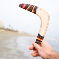 First-person view of a hand holding the Golden Swallow wooden boomerang by the painted tip, ready to throw.