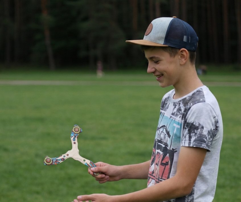 Smiling teenager holding a Seerblade wooden boomerang in a green park.