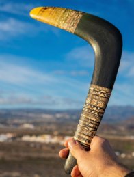 Close up of hand gripping the laser-engraved handle of a wooden boomerang.
