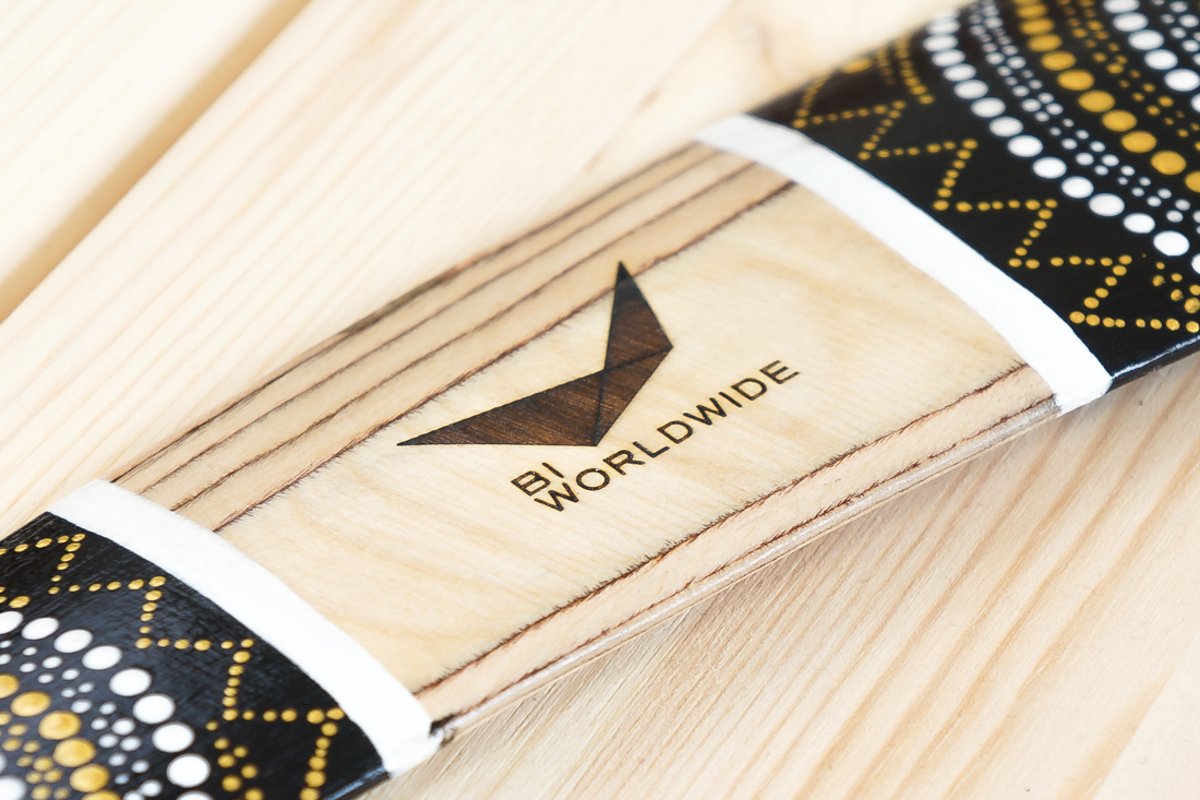 Custom wooden boomerang with laser-engraved corporate logo for BI Worldwide on natural wood center panel with hand-painted dot art