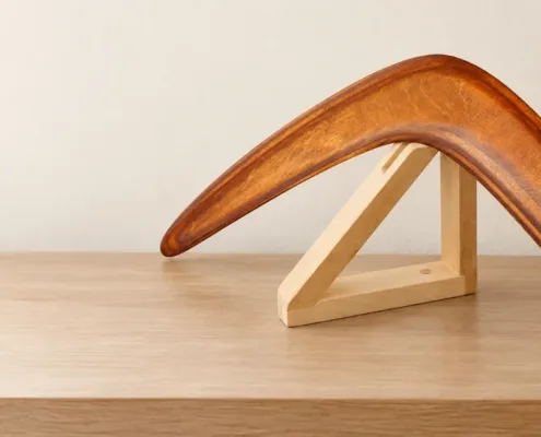 Simple care. Brown wooden boomerang displayed on a pale wooden stand indoors.