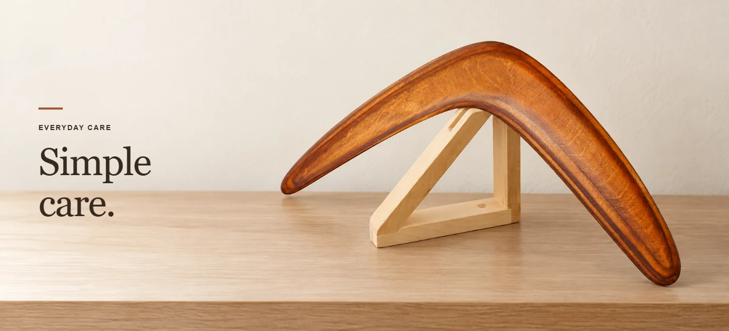 Simple care. Brown wooden boomerang displayed on a pale wooden stand indoors.