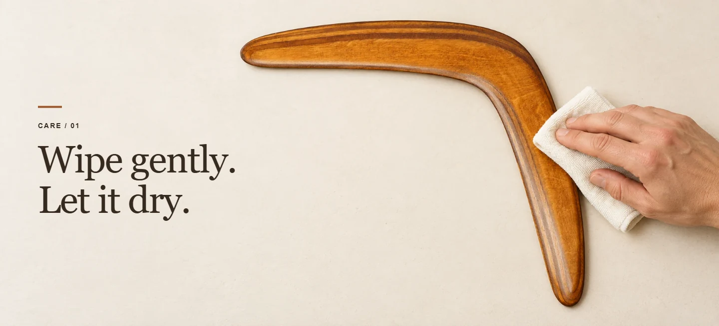Wipe gently. Let it dry. A soft cloth wiping a brown wooden boomerang on a dry surface.