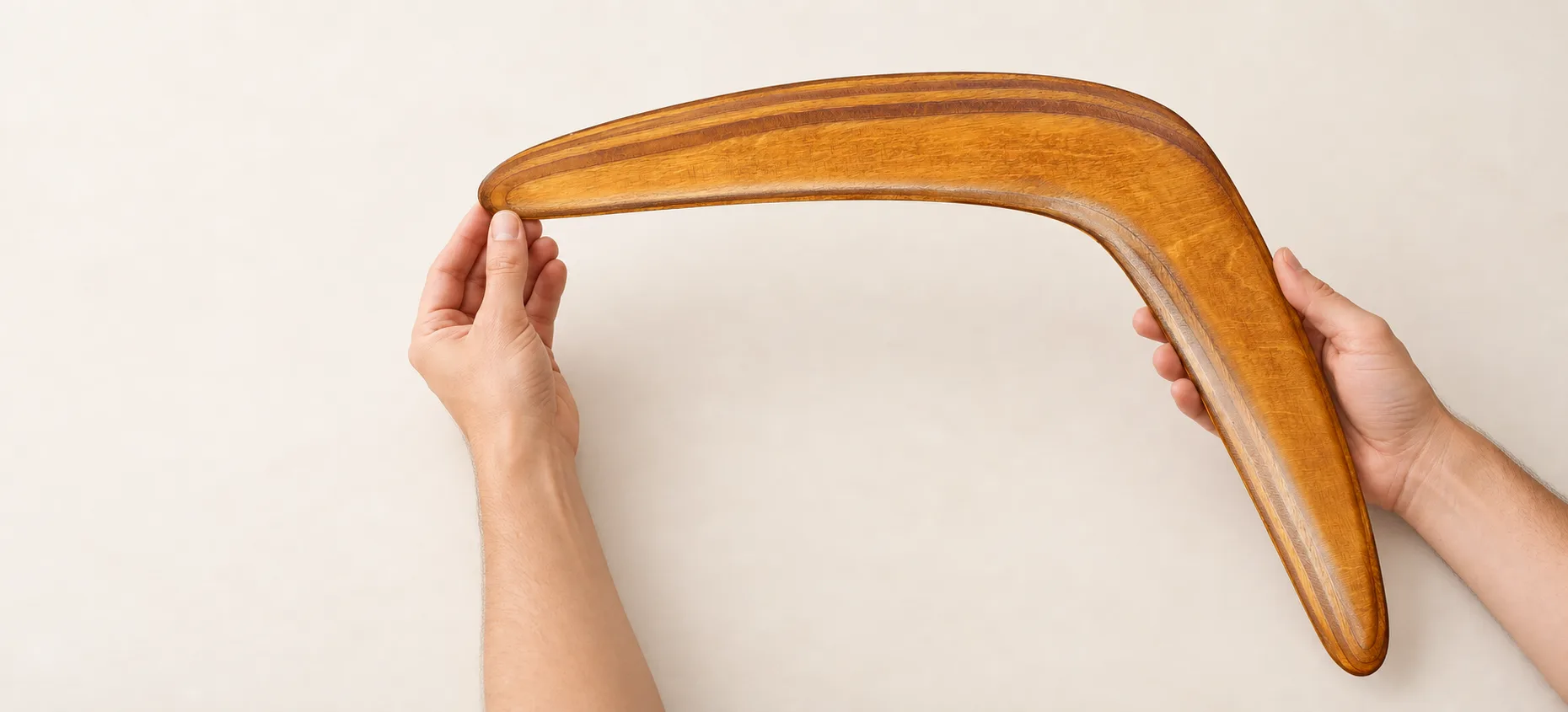 Two hands supporting a large brown wooden boomerang for inspection.